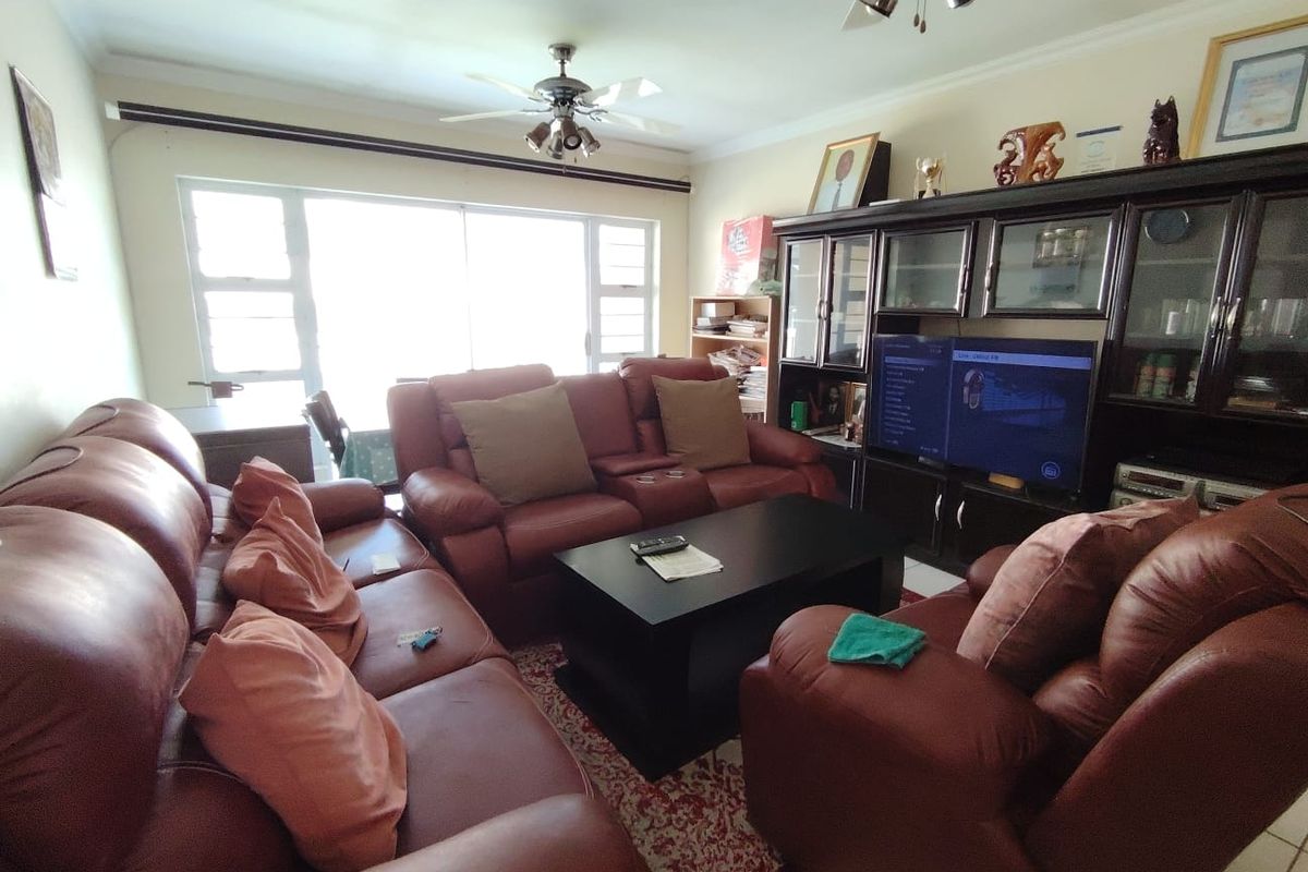 A comfortable living room featuring a ceiling fan, large windows providing natural light, and tiled flooring.