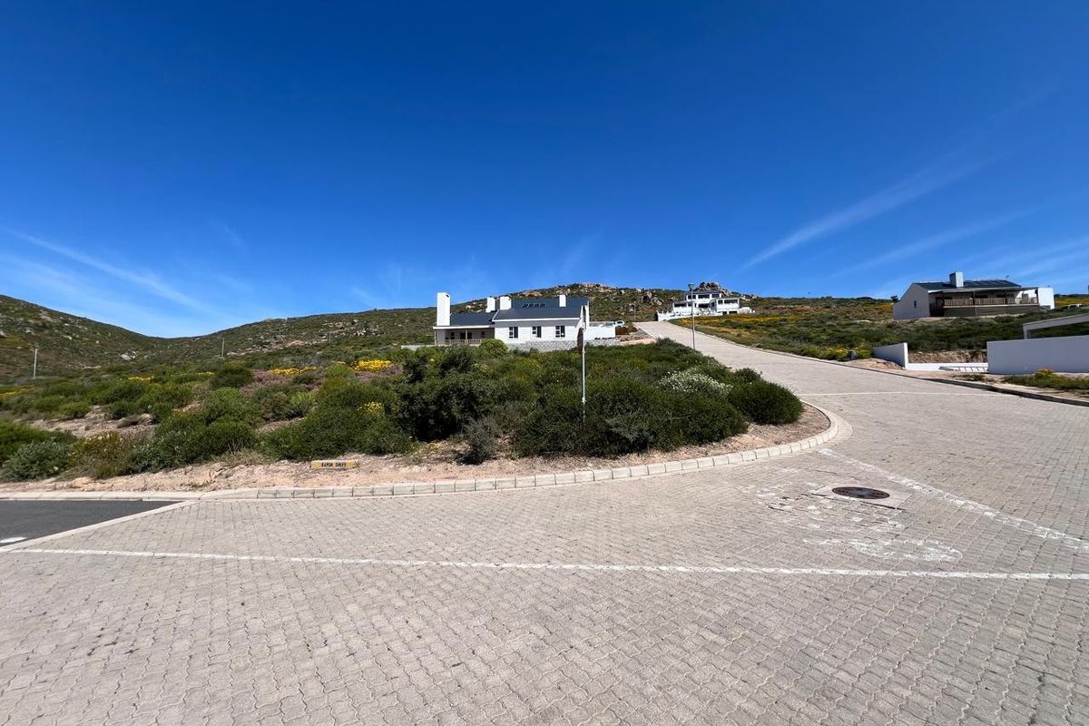 A view of the paved street approach leading up to a residential property set against a hillside landscape.