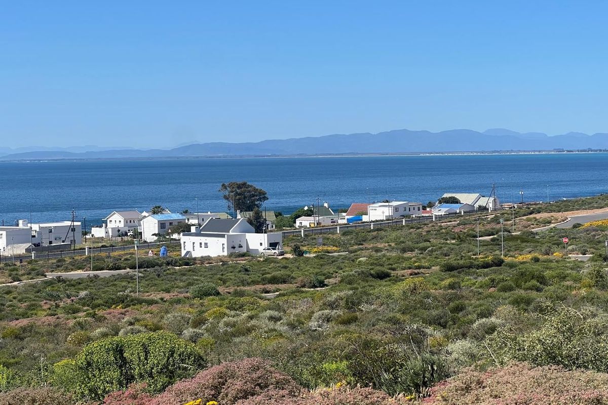 A scenic elevated view overlooking the coastal landscape, residential area, and the ocean with mountains in the distance.