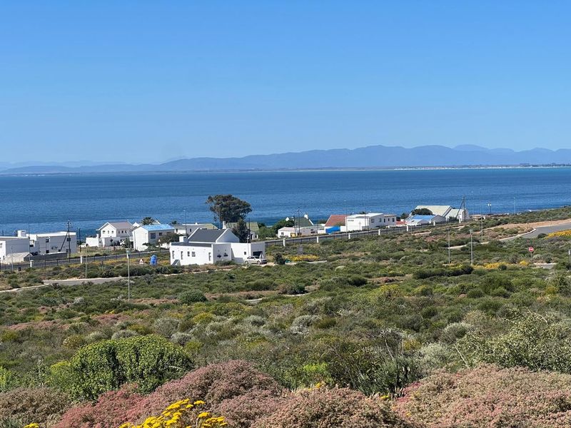 A scenic elevated view overlooking the coastal landscape, residential area, and the ocean with mountains in the distance.