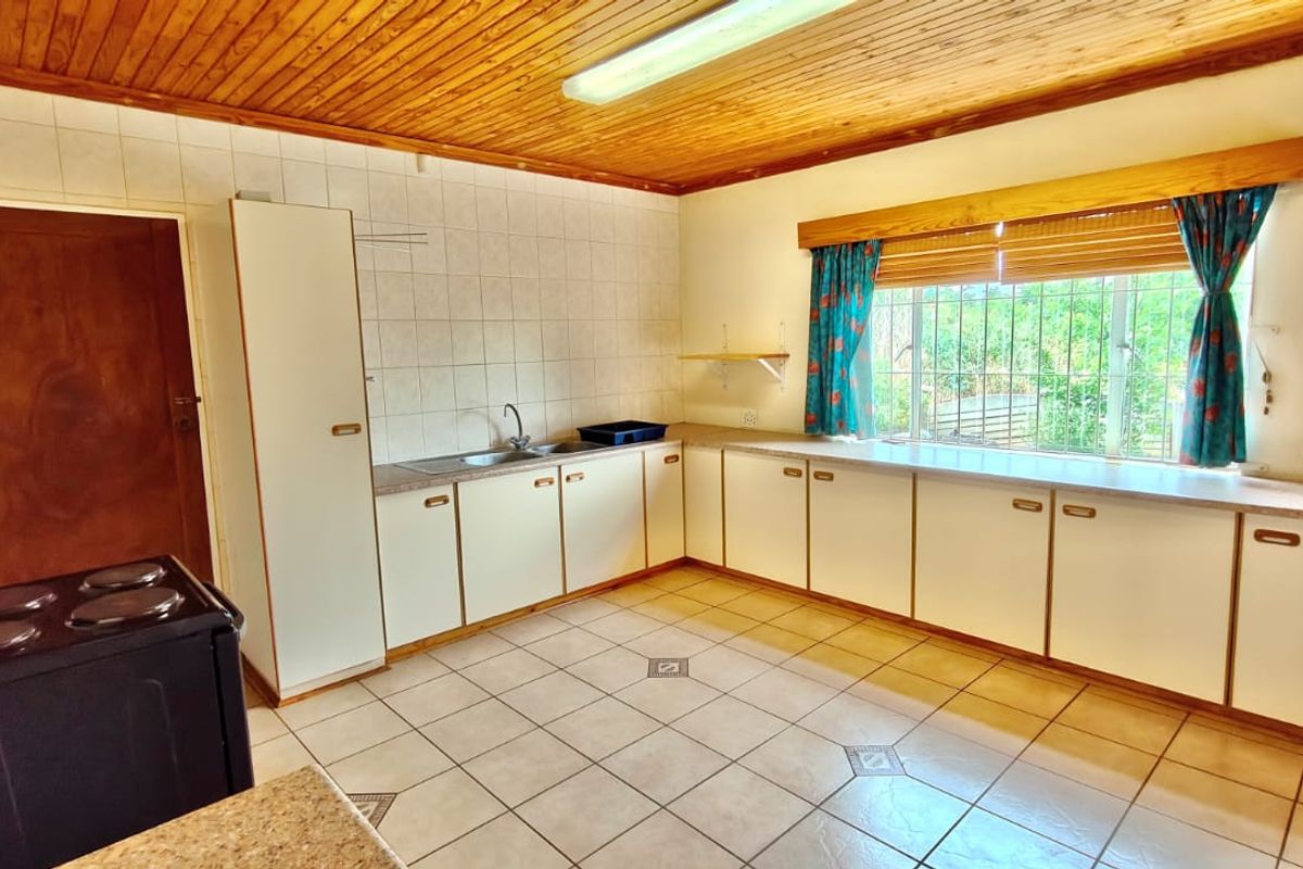 A functional kitchen featuring tiled flooring, timber ceiling, and ample laminate cabinetry with a tiled splashback and security-fitted window.
