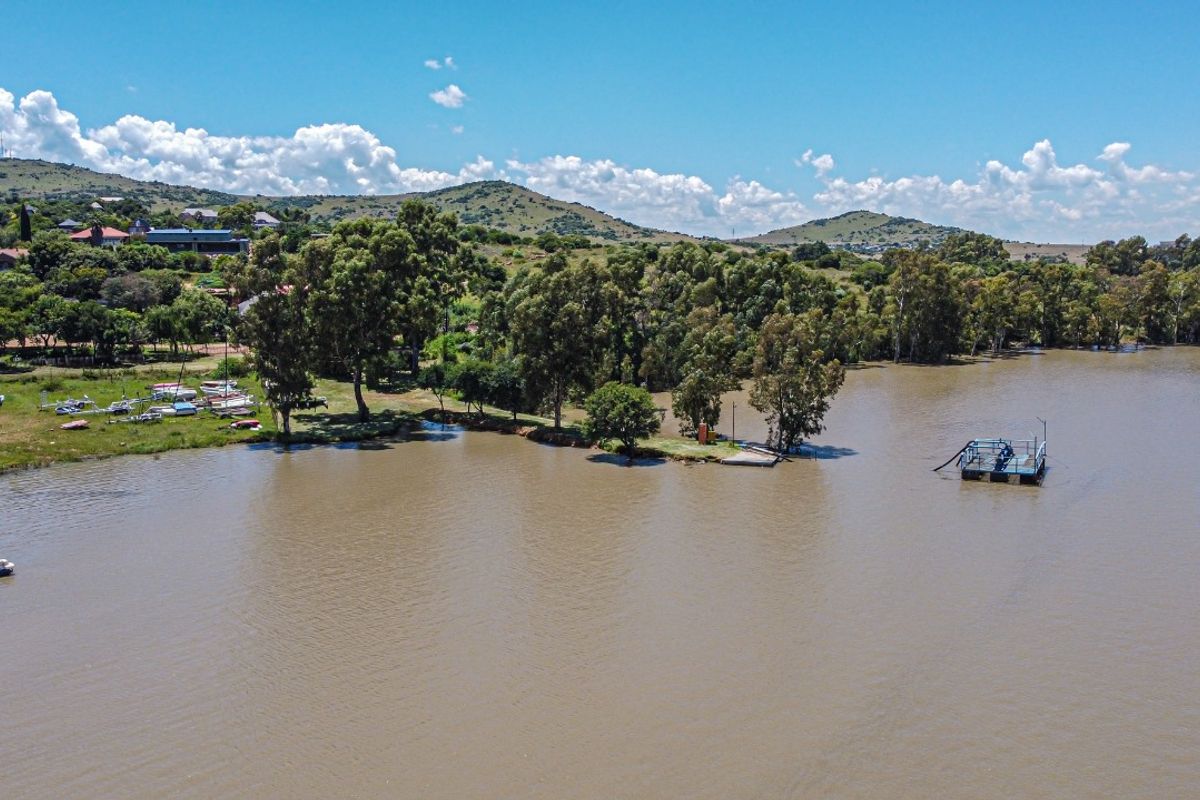 Aerial view of a lakefront property featuring a jetty, floating platform, and surrounding natural landscape with residential homes in the distance.