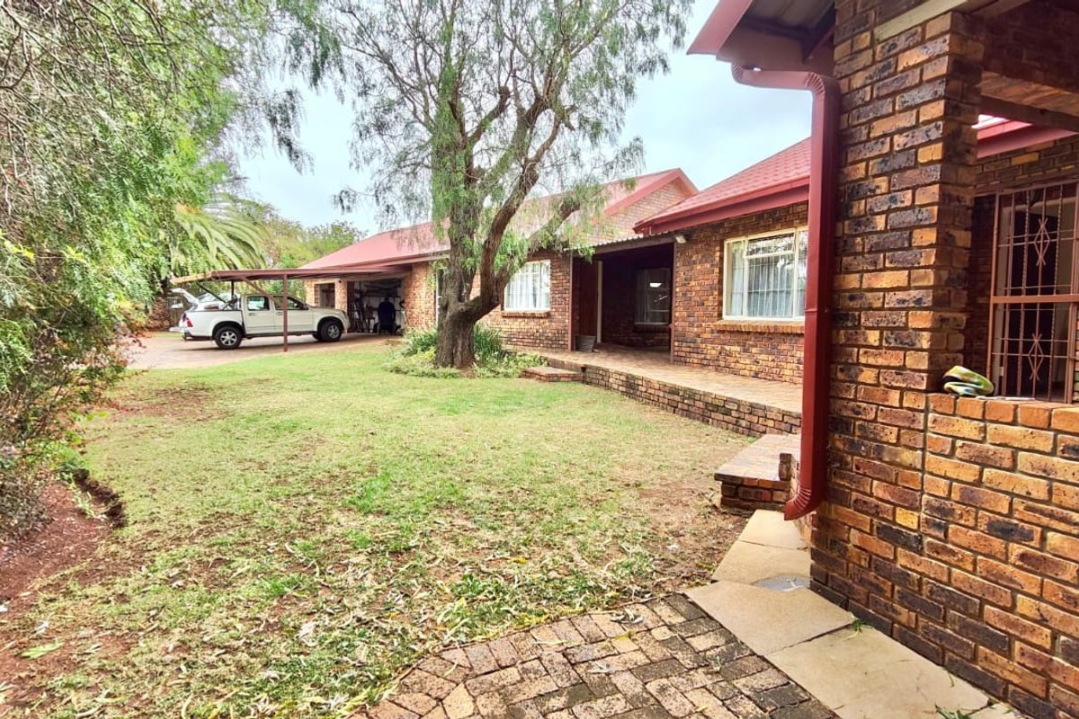 Rear view of a face brick house featuring a covered patio, paved walkway, and an attached carport area with a spacious garden.