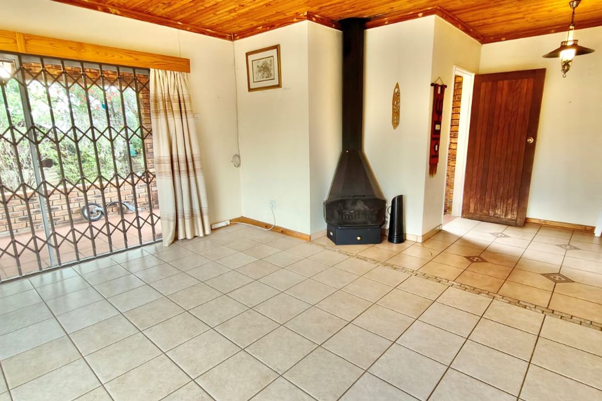 Spacious living area featuring tiled flooring, a timber ceiling, and a built-in freestanding fireplace, with direct access to the outdoor patio area.