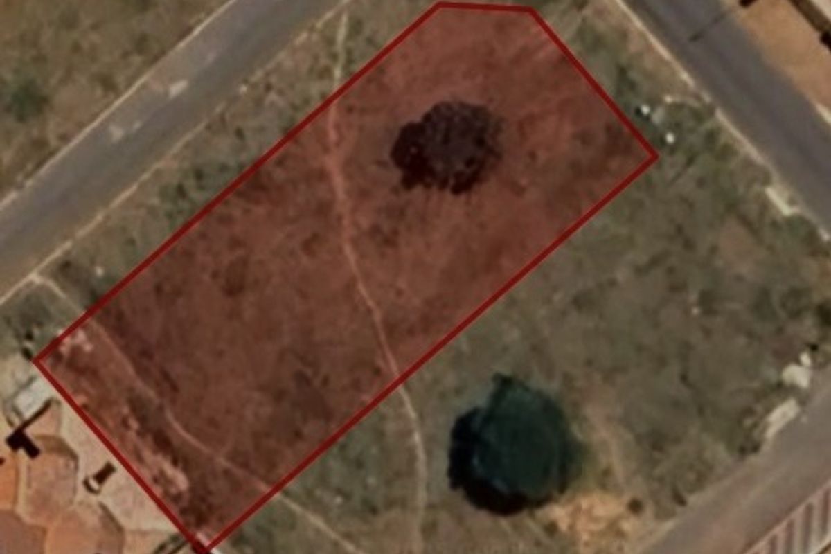 An aerial view of a vacant residential corner plot, highlighting the property boundaries and existing vegetation on the site.