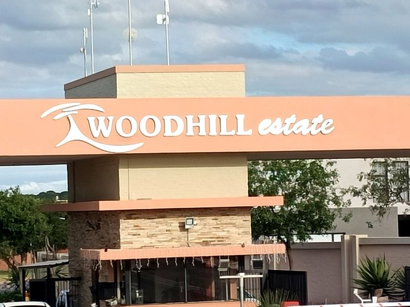The entrance gatehouse of Woodhill Estate, featuring prominent signage, stone cladding, and security infrastructure.