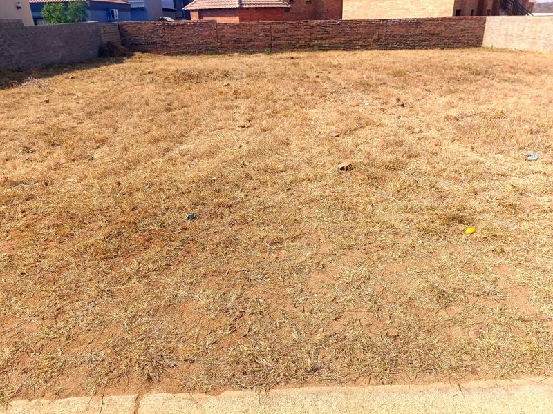 A vacant residential plot featuring dry grass and a perimeter brick boundary wall, offering a clear space for future development.