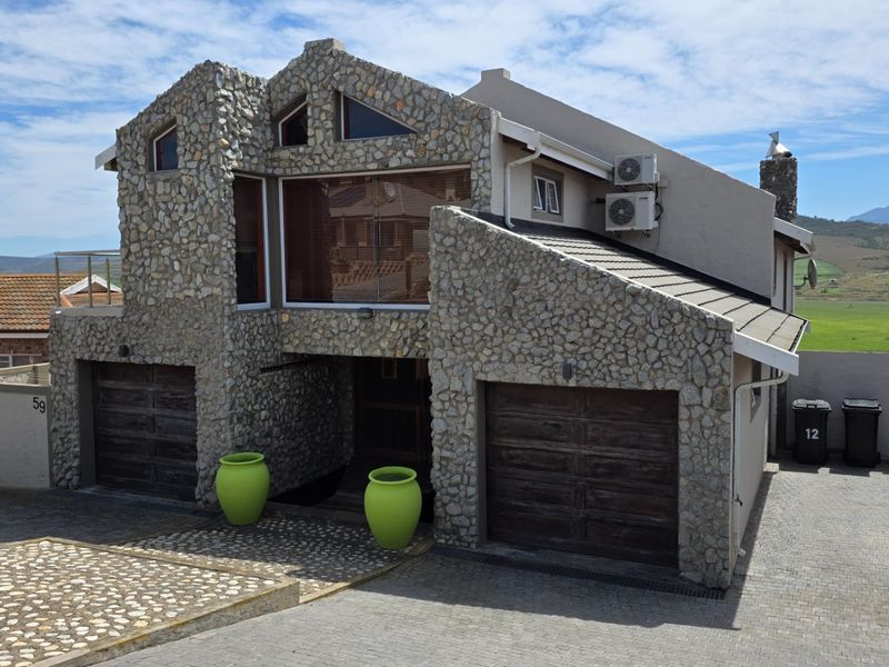 Front elevation of a multi-level residence featuring distinctive stone cladding, a double garage, and a paved driveway with mountain views.