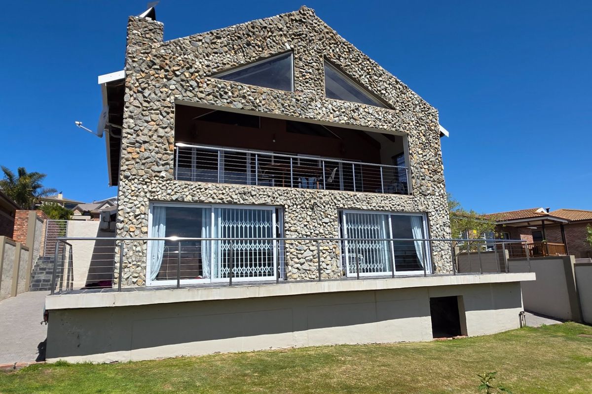 Rear view of a multi-level house featuring distinctive stone cladding, a spacious balcony with stainless steel railings, and large sliding glass doors.