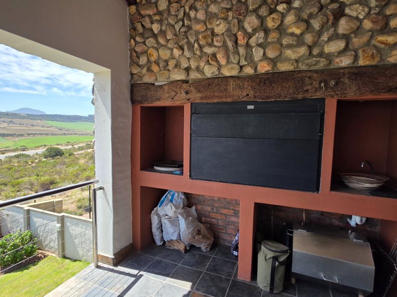 Covered patio featuring a built-in braai with stone cladding, timber beam detail, and a basin, overlooking scenic rural landscape views.