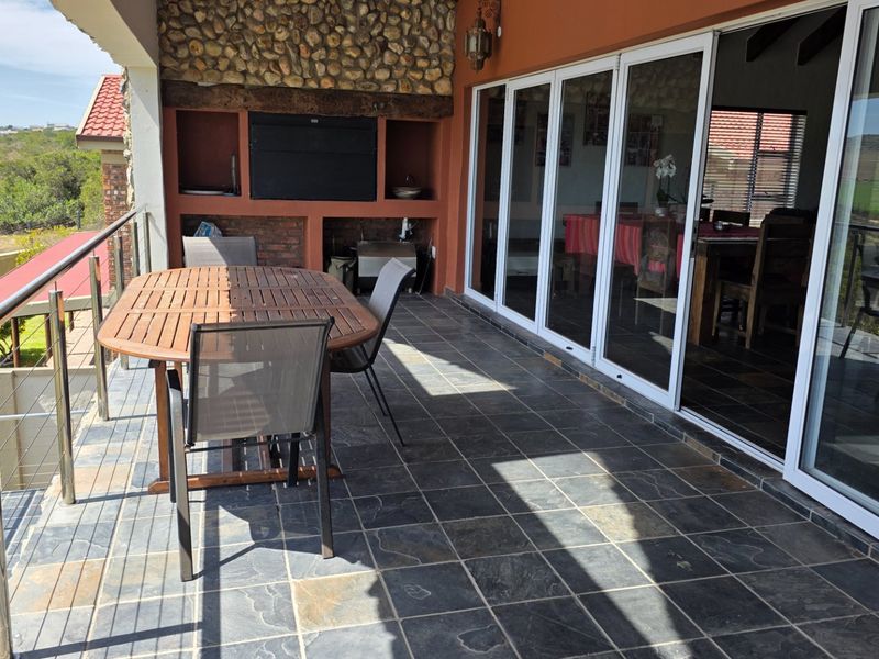 Covered patio featuring a built-in braai, stone cladding, slate flooring, and stainless steel balustrades, offering seamless indoor-outdoor flow through large sliding glass doors.