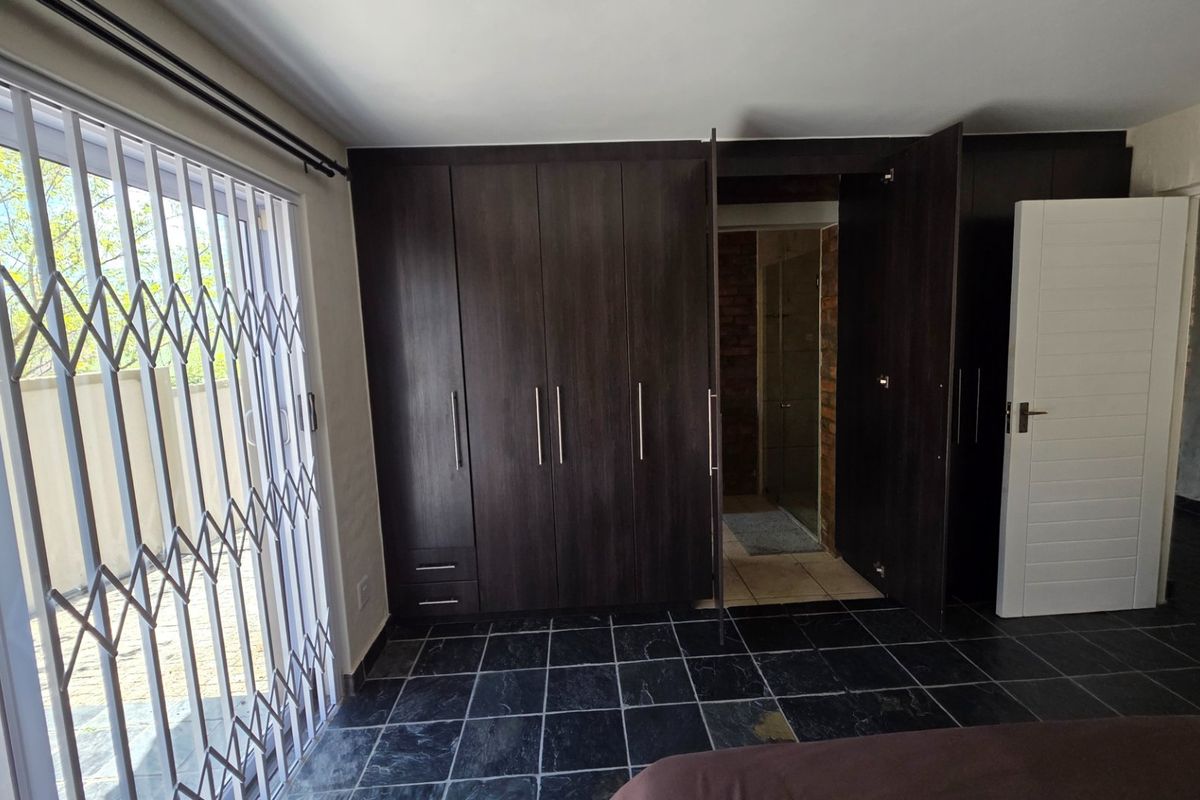Bedroom featuring dark wood built-in cupboards, tiled flooring, and direct access to an en-suite bathroom and outdoor area via a security gate.