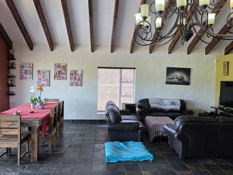 Spacious open-plan living and dining area featuring high vaulted ceilings with exposed timber beams, slate tile flooring, and a large wrought iron chandelier.