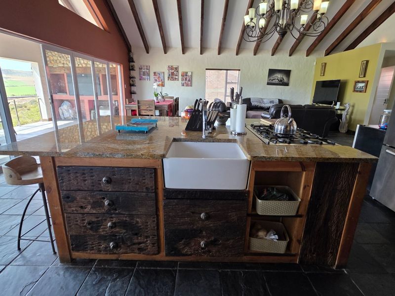 Spacious open-plan living area featuring a rustic kitchen island with granite countertop, farmhouse sink, gas cooktop, and exposed timber beams under a vaulted ceiling.