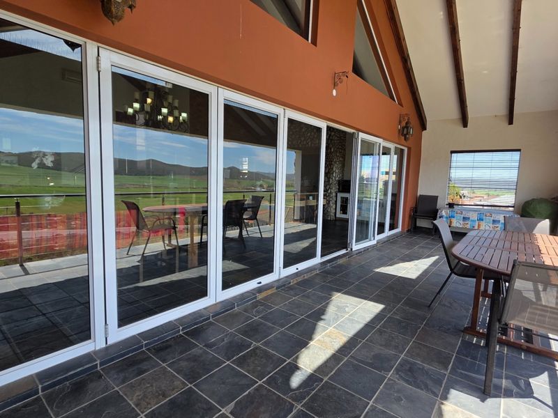 A spacious covered patio featuring slate tile flooring, exposed timber beams, and large glass sliding doors that provide seamless indoor-outdoor flow and scenic views.