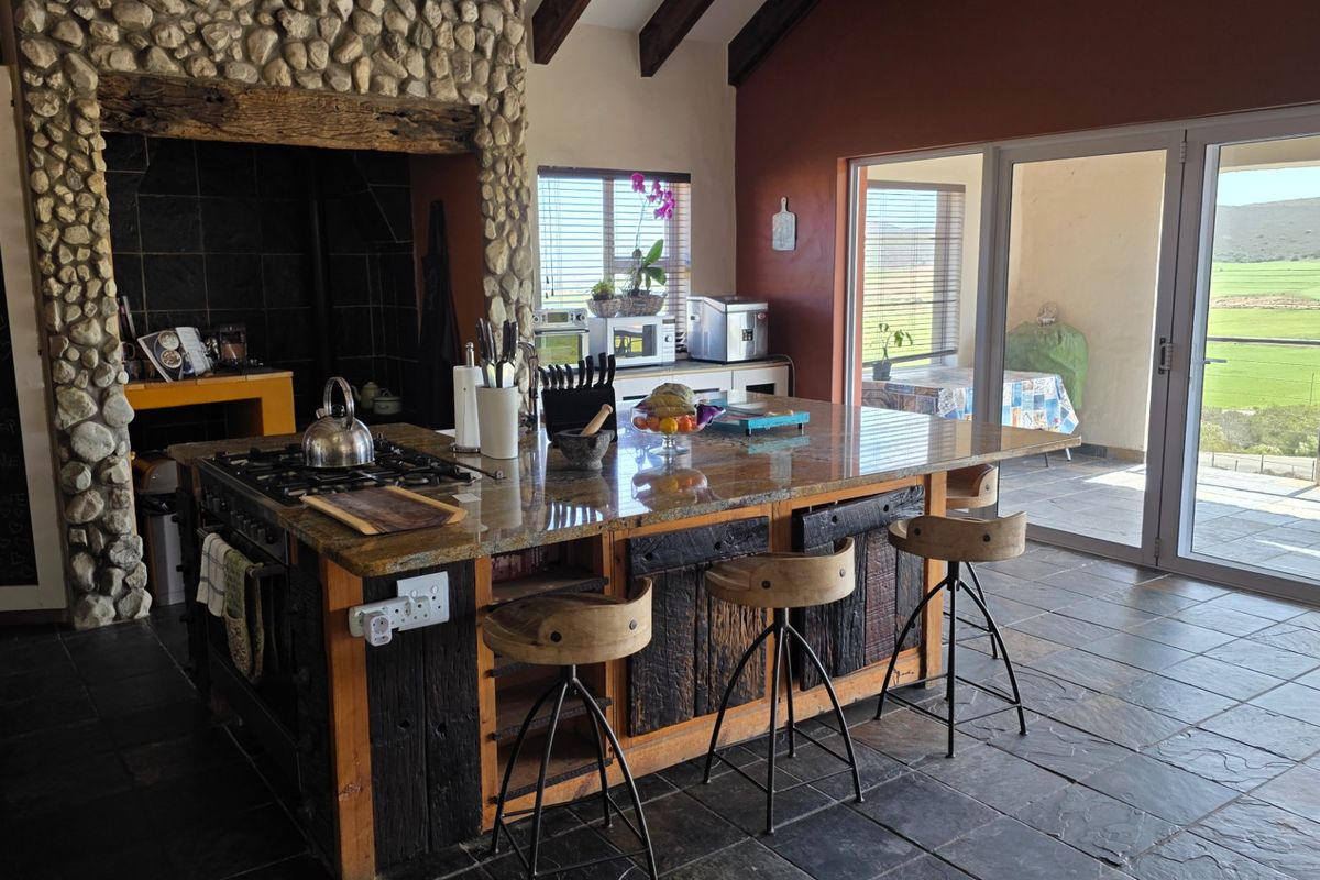 Spacious kitchen featuring a large granite island, gas hob, stone-clad fireplace, and exposed timber beams, with direct access to an outdoor patio area.