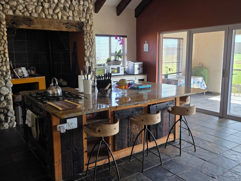 Spacious kitchen featuring a large granite island, gas hob, stone-clad fireplace, and exposed timber beams, with direct access to an outdoor patio area.