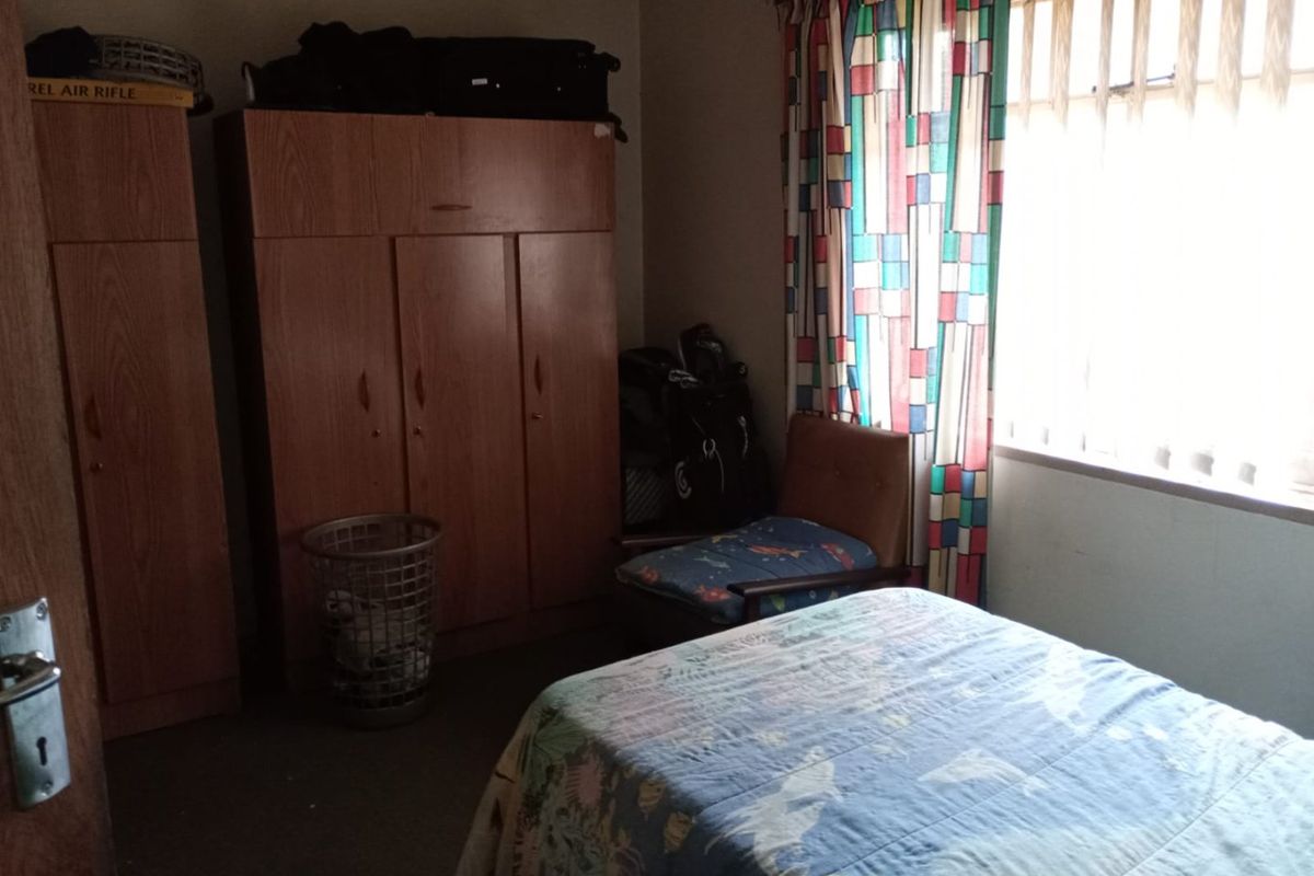 A bedroom featuring built-in wooden cupboards and a window with curtains, requiring cosmetic updates to improve the overall aesthetic and condition.