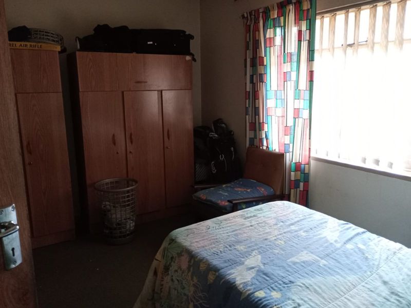 A bedroom featuring built-in wooden cupboards and a window with curtains, requiring cosmetic updates to improve the overall aesthetic and condition.