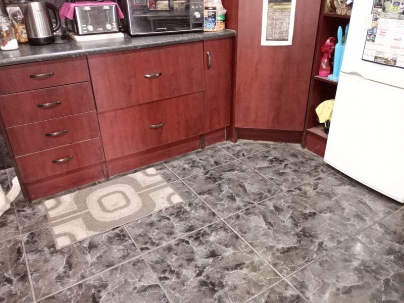 A kitchen area featuring dark wood-look cabinetry, laminate countertops, and patterned ceramic floor tiles.