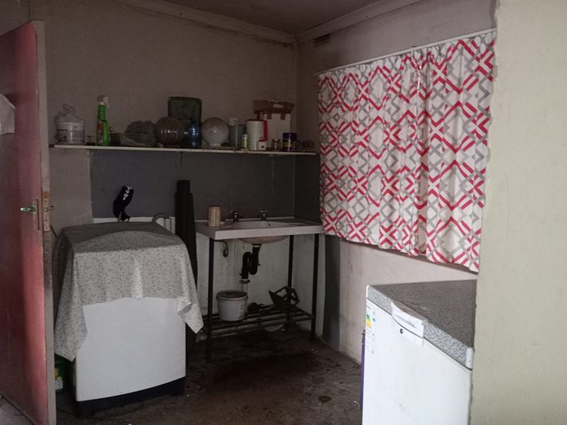 A functional laundry area featuring a utility sink, plumbing connections, and wall-mounted shelving, requiring cosmetic updates and maintenance to improve its overall condition.
