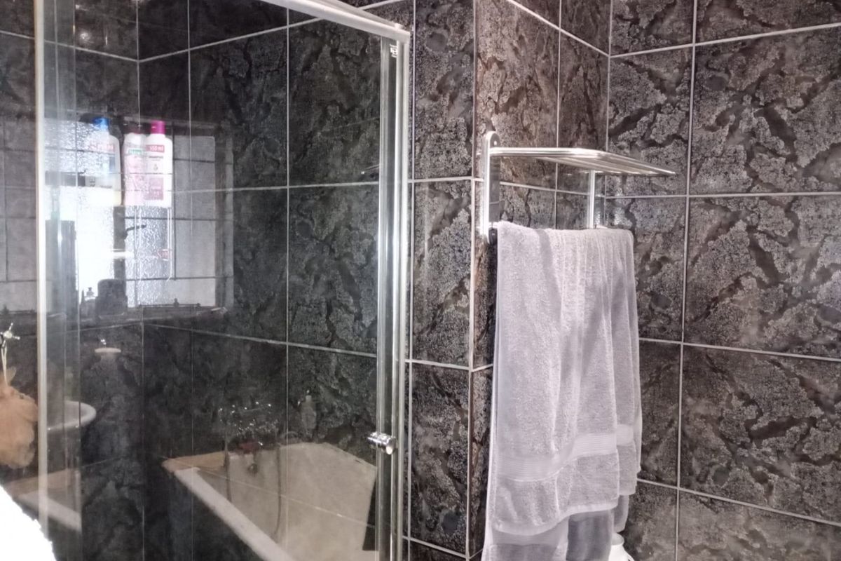 Bathroom featuring dark textured wall tiles, a glass shower enclosure, and a built-in bathtub with chrome fixtures.
