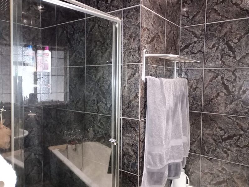 Bathroom featuring dark textured wall tiles, a glass shower enclosure, and a built-in bathtub with chrome fixtures.