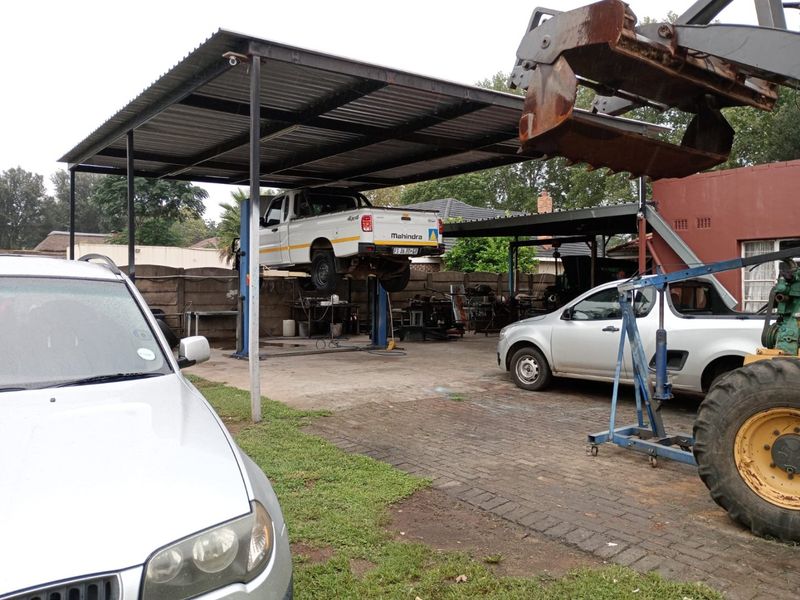 Outdoor utility area featuring a covered metal structure, paved surface, and concrete boundary wall, currently utilized for vehicle maintenance.