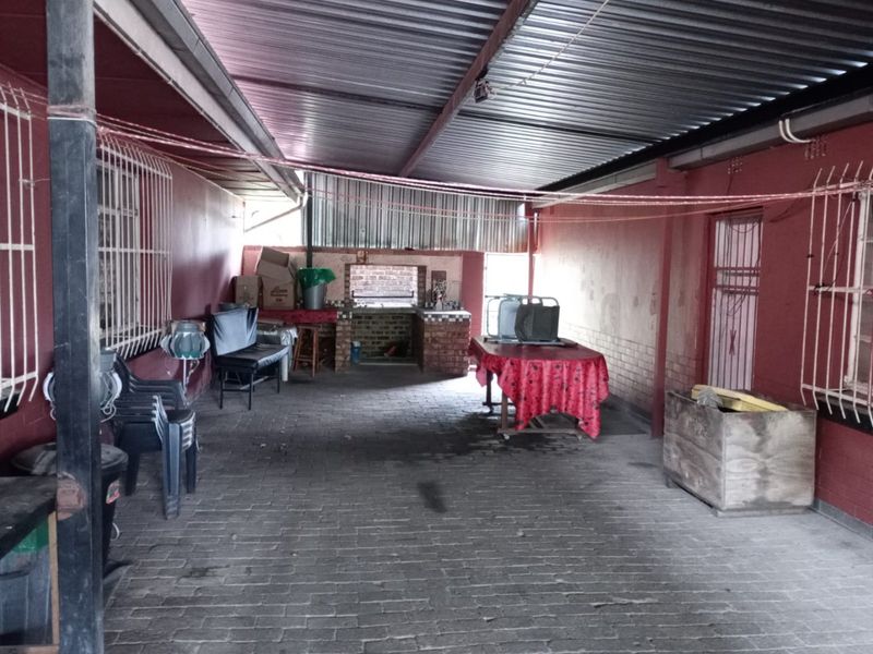 A covered outdoor patio area featuring a built-in brick braai, corrugated metal roofing, and paved flooring, suitable for outdoor entertaining.