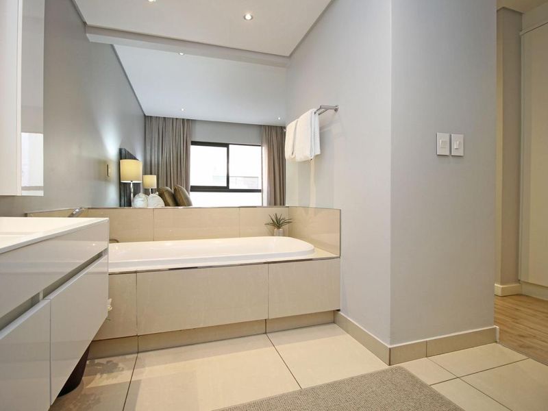 Modern bathroom featuring a built-in bathtub, sleek vanity cabinet, tiled flooring, and integrated storage cupboards in a clean, well-maintained space.