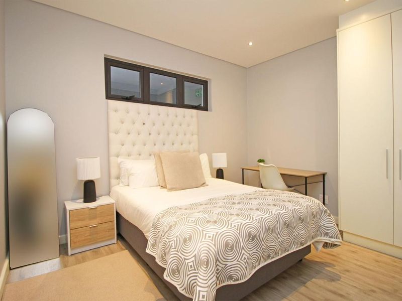A well-maintained bedroom featuring neutral tones, built-in wardrobes, recessed lighting, and modern laminate flooring.