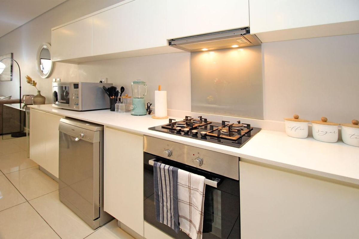 Modern kitchen featuring sleek white cabinetry, stone countertops, a gas hob, built-in oven, and a glass splashback with integrated extractor fan.