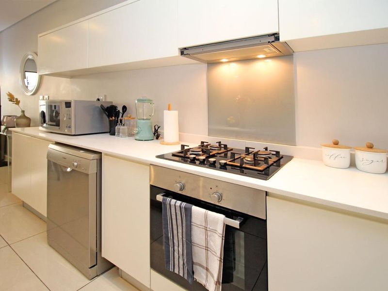 Modern kitchen featuring sleek white cabinetry, stone countertops, a gas hob, built-in oven, and a glass splashback with integrated extractor fan.