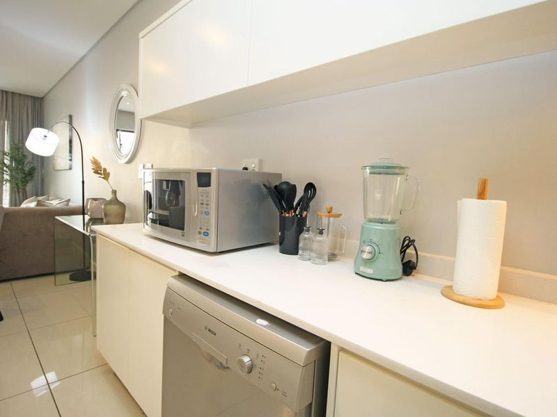 A modern kitchen area featuring sleek white cabinetry, stone countertops, and integrated appliances, seamlessly flowing into the adjacent living space.