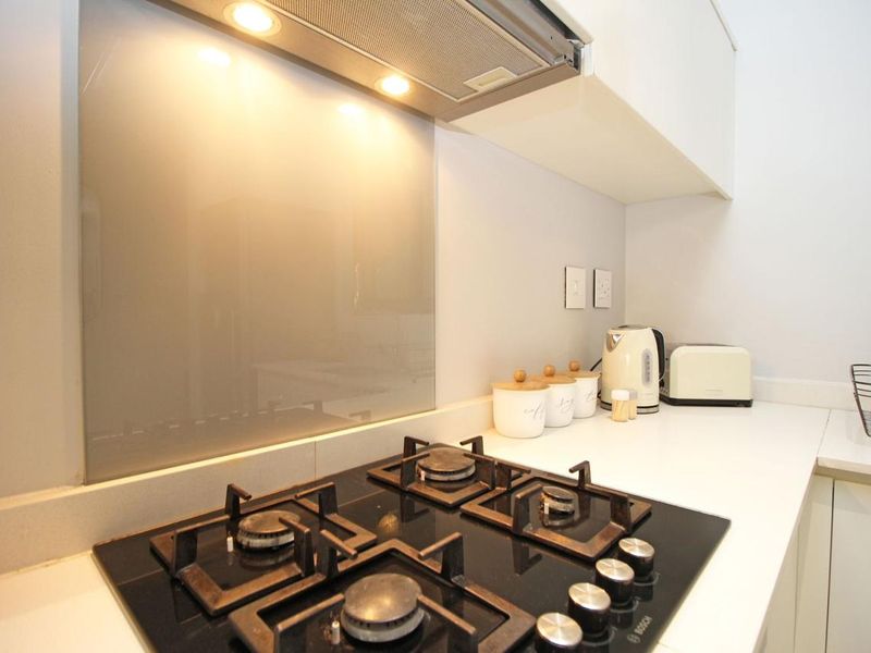 A modern kitchen area featuring a sleek black gas hob, integrated extractor fan, and a clean glass splashback with stone countertops.