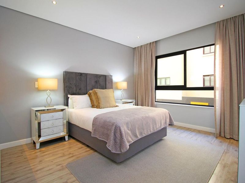 A well-maintained bedroom featuring modern laminate flooring, recessed downlighting, and large aluminium-framed windows with neutral curtains.