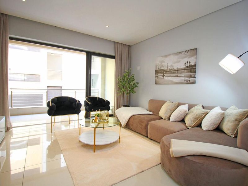 A bright and modern living room featuring large sliding glass doors that open onto a balcony, complemented by neutral tiled flooring and recessed lighting.