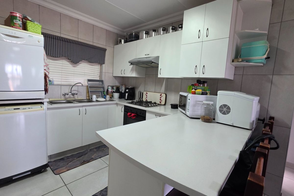 A functional kitchen featuring white built-in cabinetry, a gas hob with extractor fan, double sink, and a breakfast counter with tiled finishes.