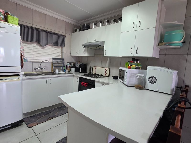 A functional kitchen featuring white built-in cabinetry, a gas hob with extractor fan, double sink, and a breakfast counter with tiled finishes.