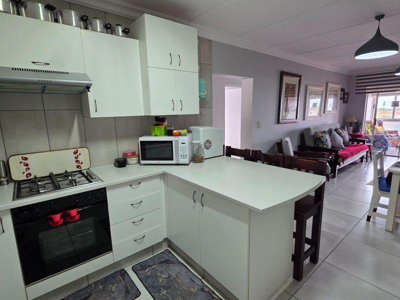 An open-plan kitchen and living area featuring white cabinetry, a gas hob, built-in oven, and tiled flooring, leading to a balcony with natural light.