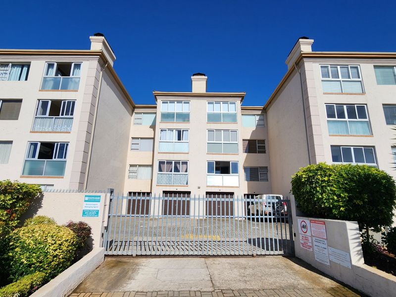 Front elevation of a multi-story apartment complex featuring a secure gated entrance, paved driveway, and well-maintained exterior facade.