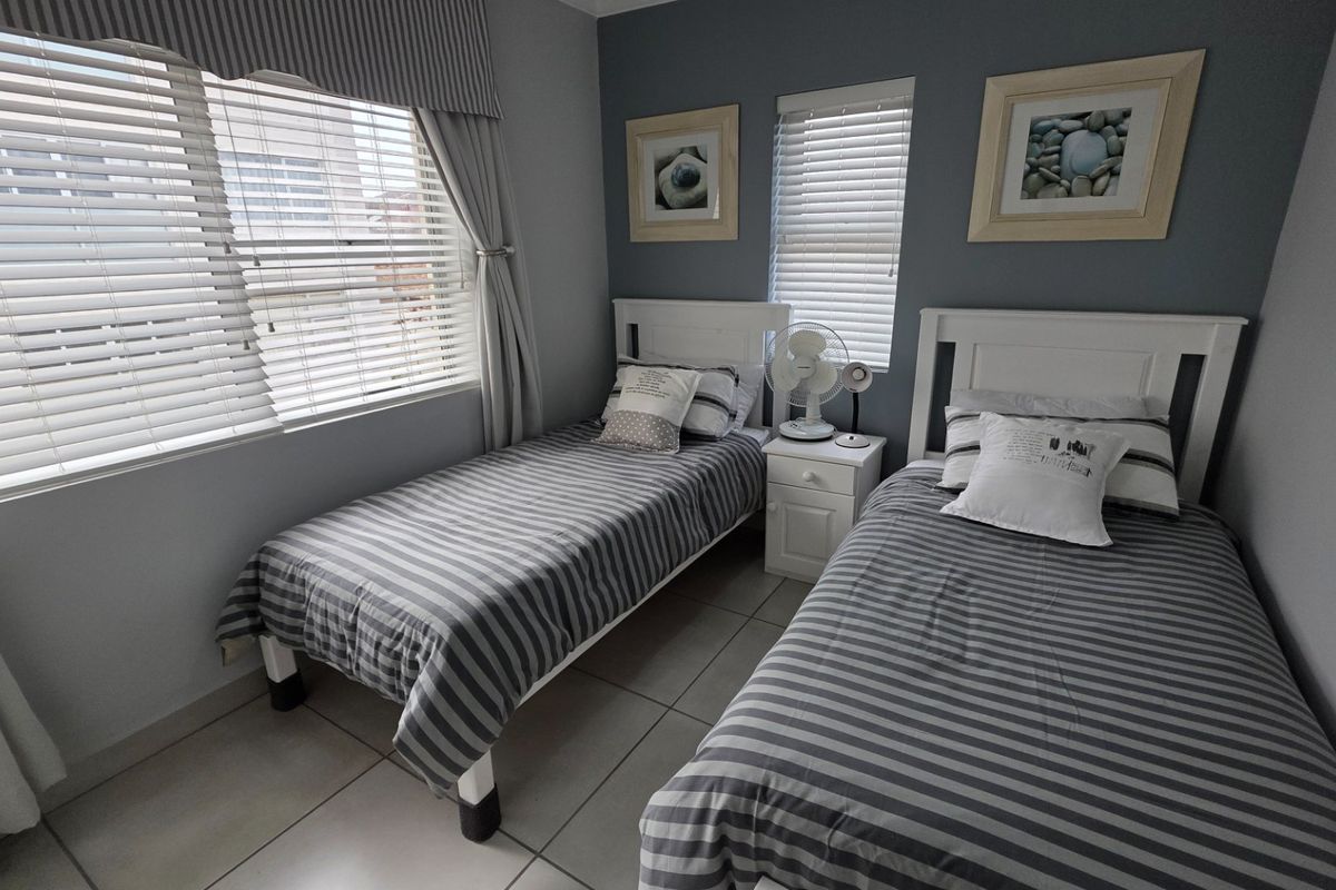 A well-maintained bedroom featuring neutral tiled flooring, dual windows with fitted venetian blinds, and a coordinated curtain pelmet.