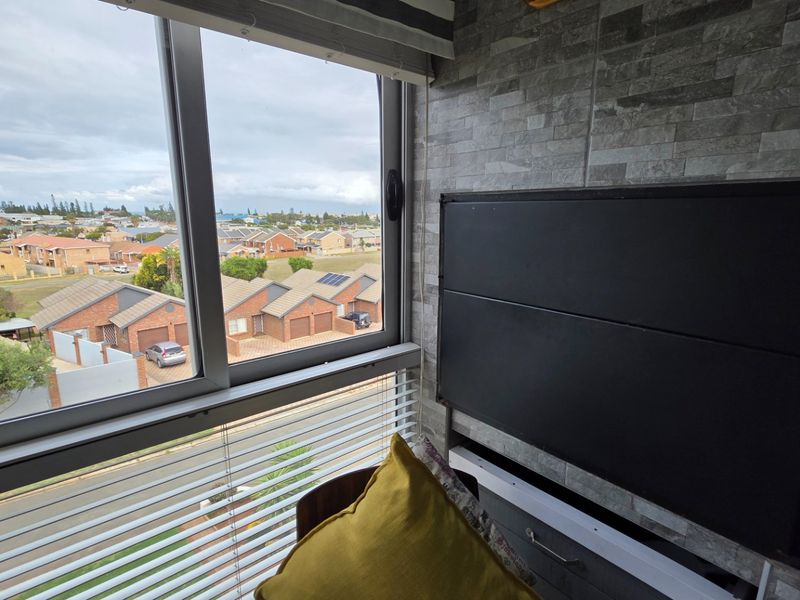 Enclosed balcony area featuring stone-clad walls, aluminium window frames, and venetian blinds, offering an elevated view of the surrounding residential neighbourhood.