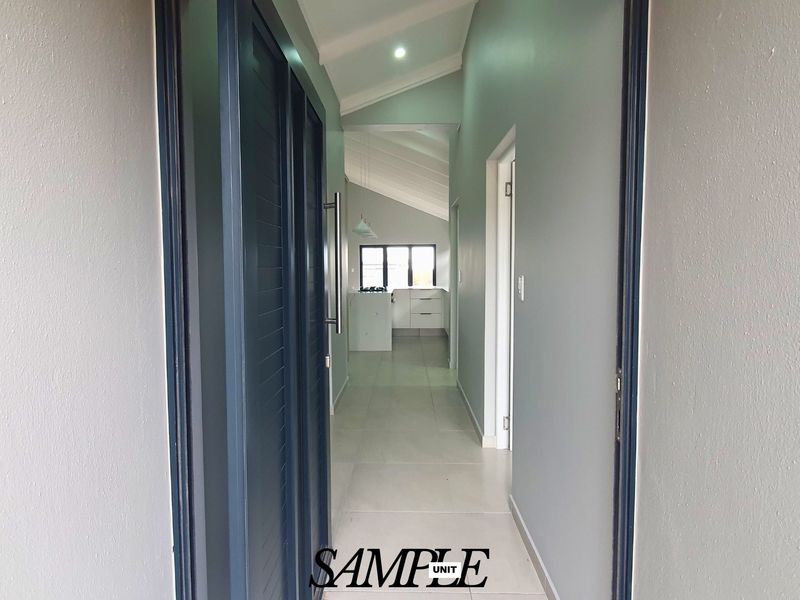 A bright, modern hallway with tiled flooring and a vaulted ceiling, leading towards an open-plan kitchen area.
