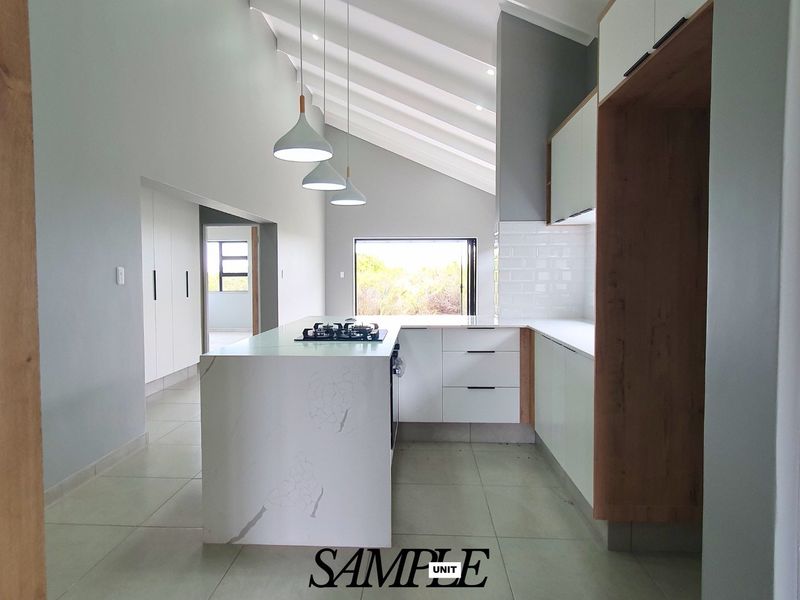 Modern kitchen featuring a central island with a gas hob, sleek white cabinetry, subway tile backsplash, and a high vaulted ceiling.