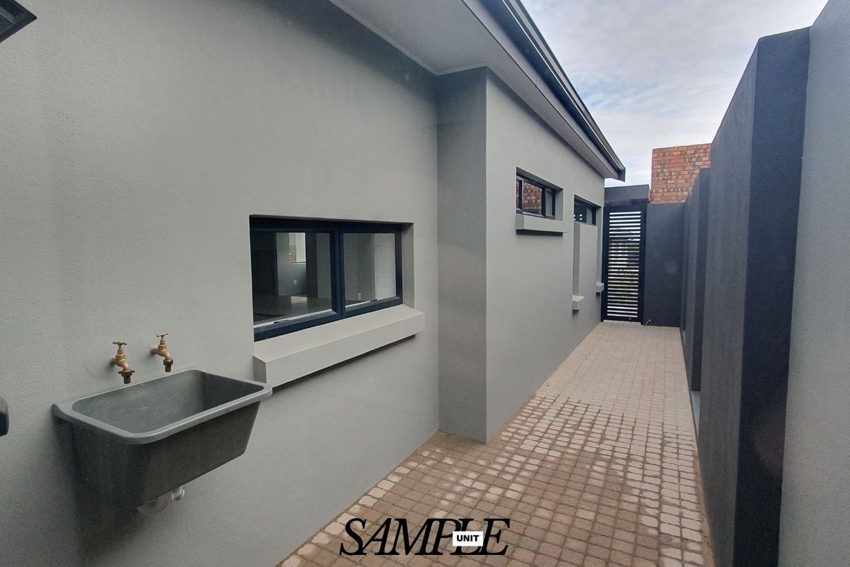 A clean, modern side exterior walkway featuring a utility sink, paved flooring, and secure boundary walls.