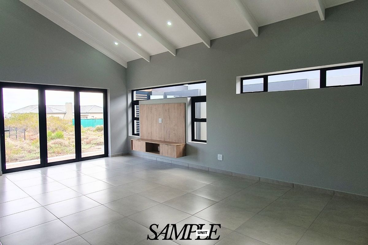 Spacious living area featuring vaulted ceilings, tiled floors, built-in media cabinetry, and large sliding doors providing ample natural light.