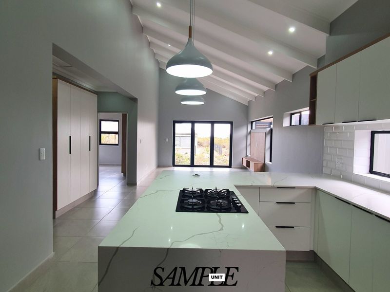 Modern open-plan kitchen and living area featuring a large island with gas hob, sleek cabinetry, vaulted ceilings, and abundant natural light.