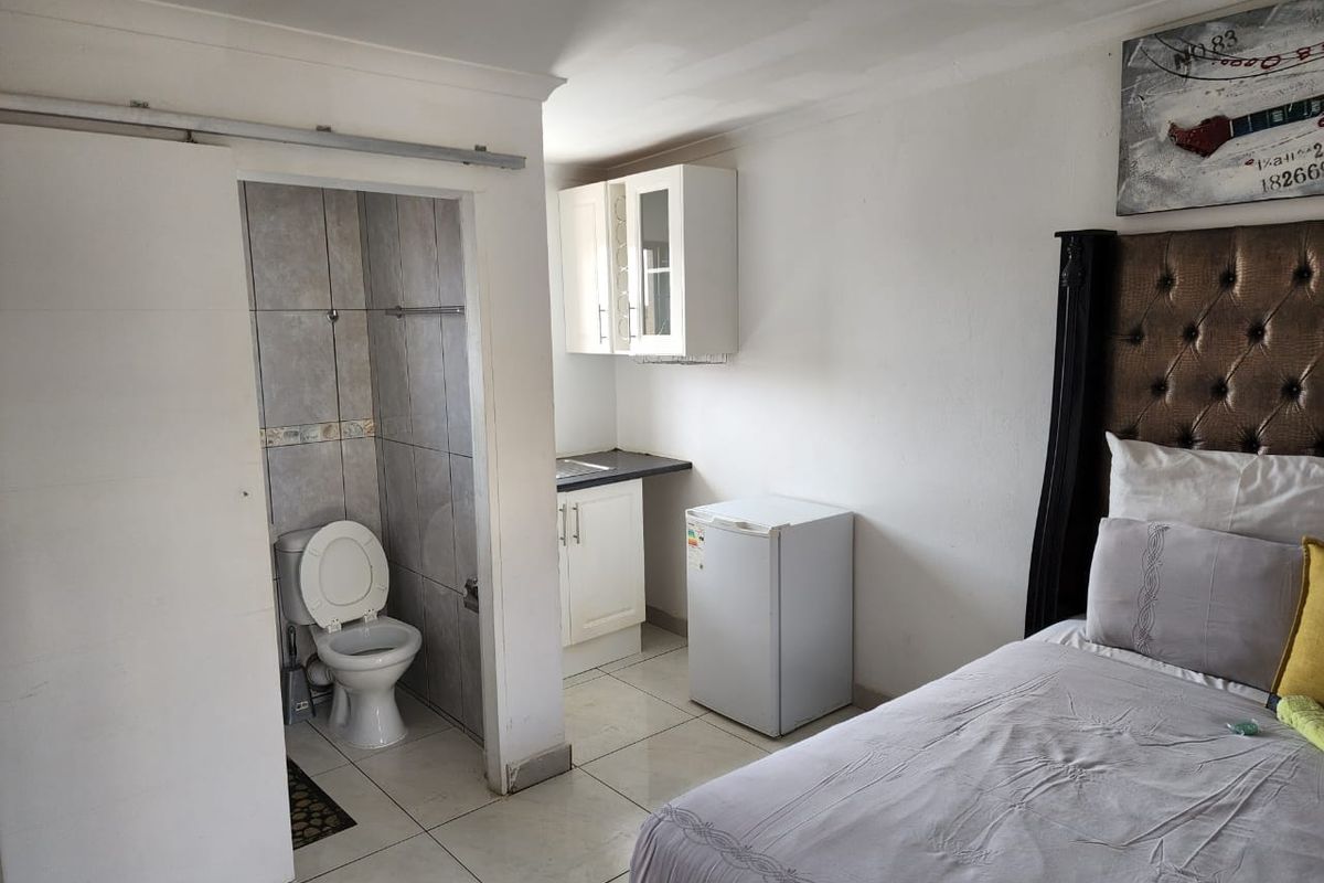 A bedroom featuring an integrated small kitchenette and an en-suite toilet, with tiled flooring and basic cabinetry.