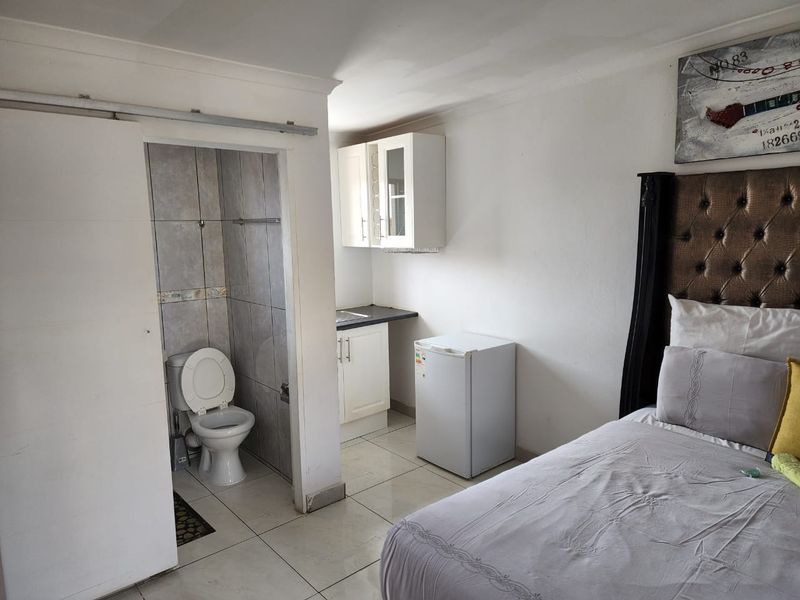 A bedroom featuring an integrated small kitchenette and an en-suite toilet, with tiled flooring and basic cabinetry.